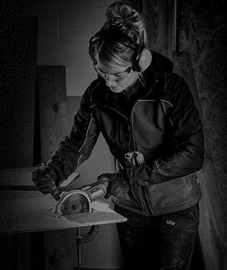 A woman cutting a wooden board with a saw